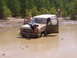 1995 Ford Bronco - A Ford Bronco is stuck in a mud pit with two people on the hood and in the driver's seat.