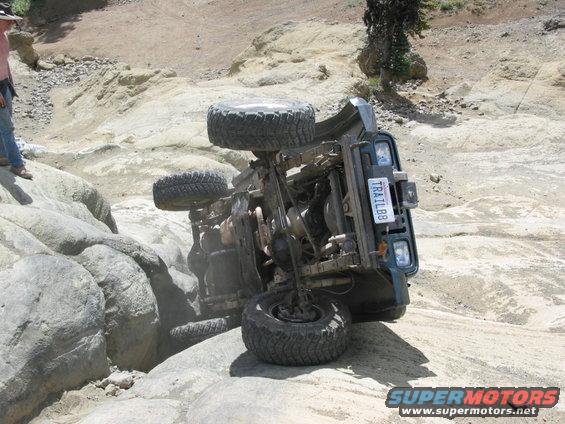 Off-road vehicle flipped onto its side on a rocky trail. License plate reads TRAIL88