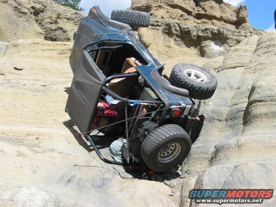 Overturned dark green off-road vehicle on rocky terrain, spare tire visible on roof