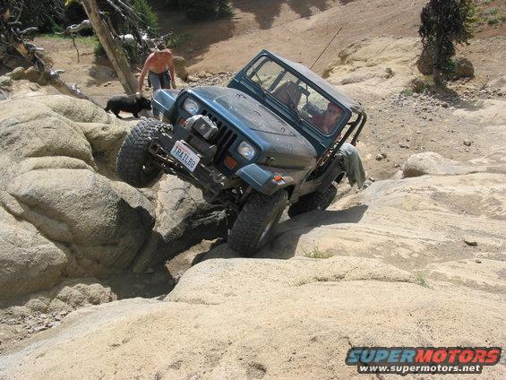 Teal Jeep Wrangler navigating rocky terrain, front license plate reads TRAILBB