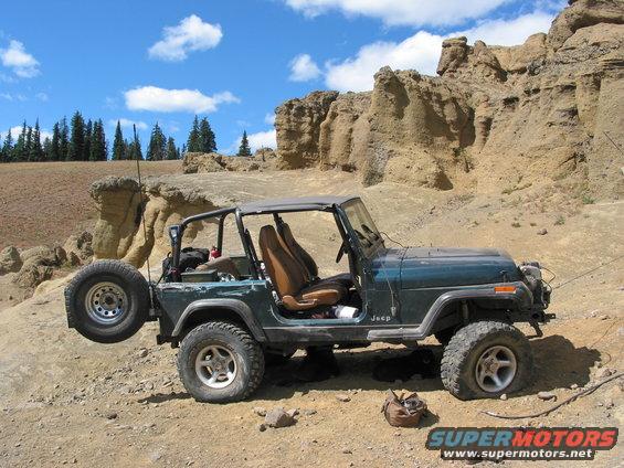 Green Jeep Wrangler parked on rocky terrain with spare tire mounted on rear
