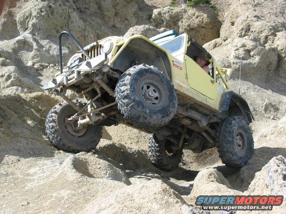 Yellow jeep climbing rocky terrain, driver visible inside