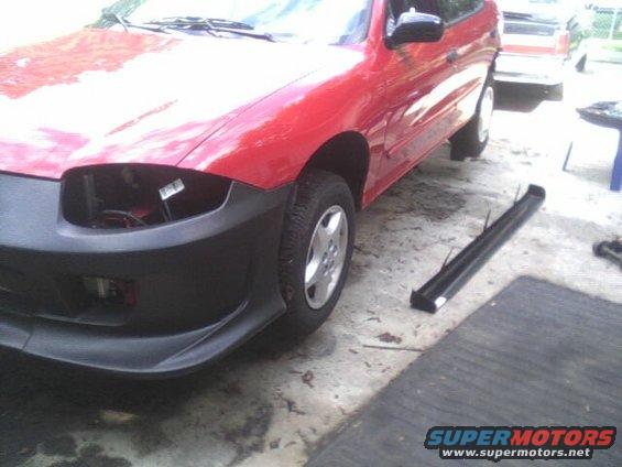 Red car, front bumper removed, missing headlight. Another vehicle is parked behind it