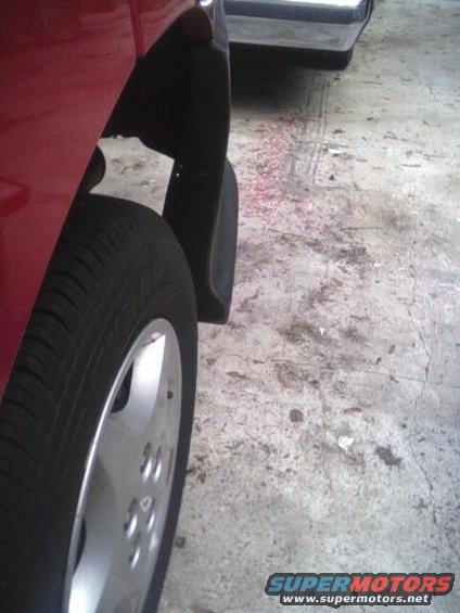 Close-up of a red car's front wheel and fender. Another vehicle is parked behind it