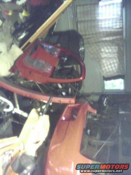 red car bumper and headlight assembly in a cluttered garage