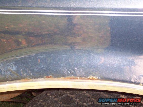 Close-up of rusted metal on a vehicle's wheel well with a tire visible below