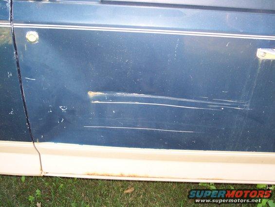 Blue vehicle door with chrome trim, showing significant scratches and a dent near the handle
