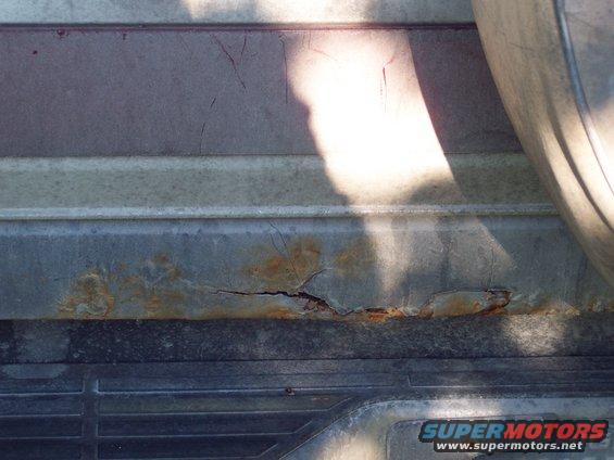 Close-up of rusted metal on a vehicle body panel, showing cracked paint and corrosion