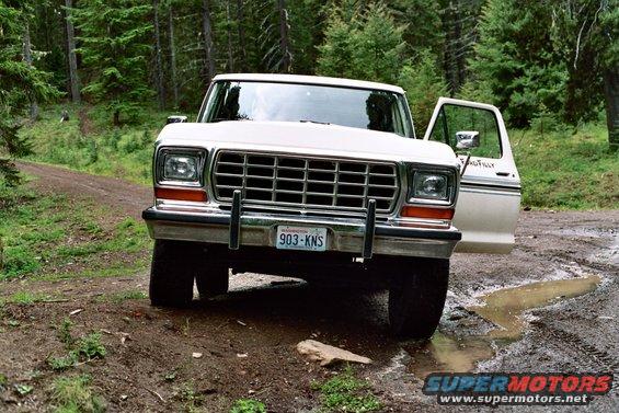 1979 Ford Bronco parked on a muddy dirt road in a forest, driver's door open