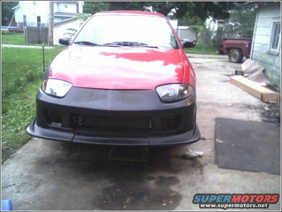 Red car with aftermarket black front bumper and lip kit, parked on concrete