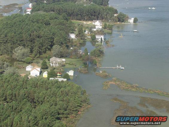 Aerial view of flooded coastal homes and trees, with a dock and boats in the water