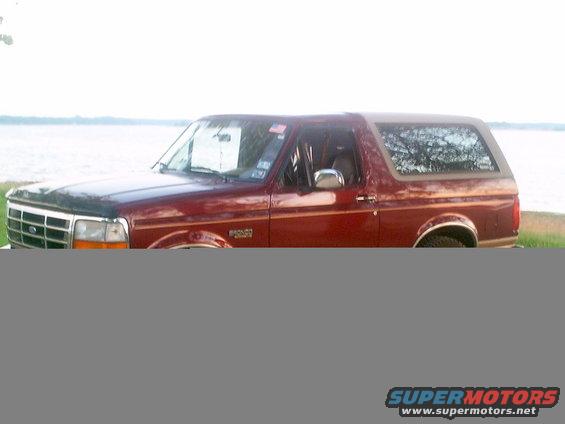Red 1996 Ford Bronco parked by a body of water, showing its side and front quarter panel