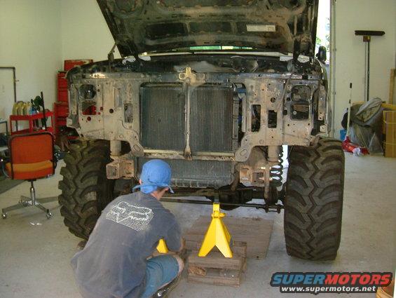 Truck front end disassembled with hood up, radiator removed. Person in blue hat working on it