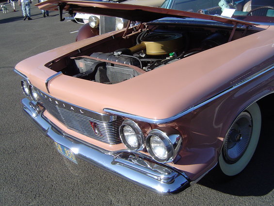 Front view of a pink 1960 Imperial with hood open, showing engine. Chrome grille and headlights visible