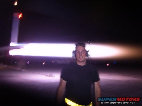 Man wearing headphones stands in front of a bright light source, possibly a jet engine exhaust