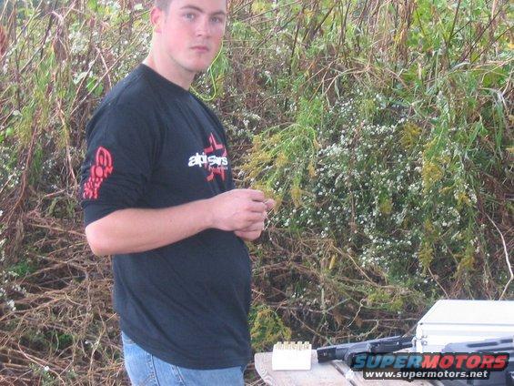 Man holding ammunition with a gun and ammo box on a table outdoors