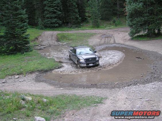Dark pickup truck navigating a muddy turn on a dirt road