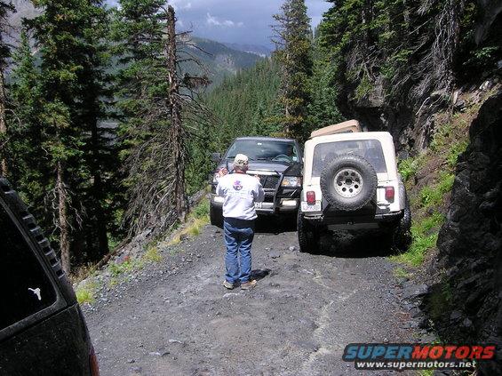 Two off-road vehicles stopped on a narrow, rocky mountain road with a person standing between them