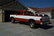 1993 Dodge 2500 - A red and white Dodge pickup truck is parked in a driveway next to a garage. Another vehicle is visible behind it.