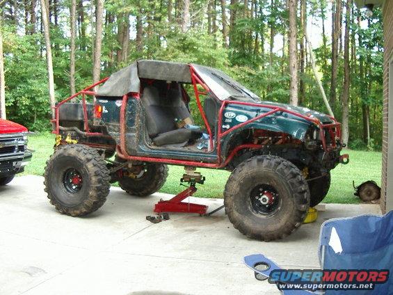 Modified off-road vehicle with roll cage, large tires, and no doors, jacked up for maintenance