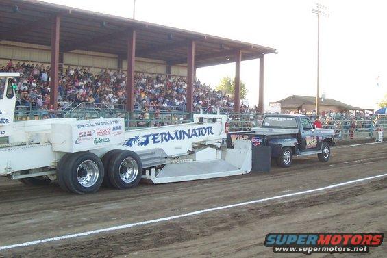 Black pickup truck pulling a trailer labeled "TERMINATOR" at a drag race
