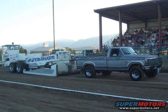 Gray Ford pickup truck, 1980s model, towing a white implement labeled "TERMINATOR"