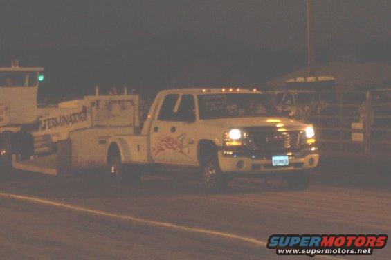White GMC pickup truck with a tow bed, graphics on the door, driving at night