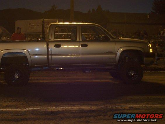 Lifted crew cab pickup truck with large tires, seen from the side at night