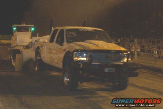 White pickup truck with flames and a tow truck at night. Text on windshield reads '05'