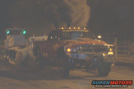 Red Dodge pickup truck blowing black smoke, pulling a trailer. Text on windshield says "BigBadDodge"