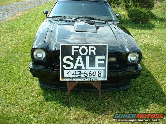 Black 1978 Ford Mustang II, front view, with a 'For Sale' sign on a stand in front