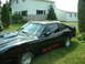 1978 Ford Mustang II - A black coupe with a distinctive rear window louvers and a flame decal is parked on a grassy lawn in front of a house.