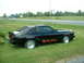 1978 Ford Mustang II - A black 1978 Ford Mustang II coupe is parked on the grass next to a highway, distinctive rear window louvers and side decals.