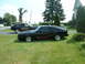 1978 Ford Mustang II - Two black Ford Mustang IIs are parked on a grassy lawn in front of a house and trees.