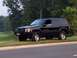 1996 Jeep Grand Cherokee - A black 1996 Jeep Grand Cherokee is parked on a grassy area next to a road, with trees in the background.