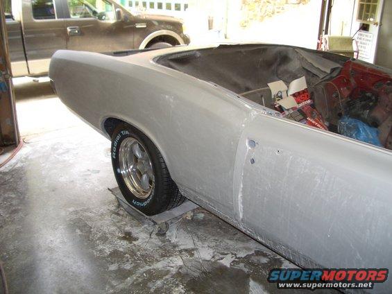 1967 Pontiac GTO convertible body in primer, rear quarter panel and wheel visible, interior partially exposed, truck in background