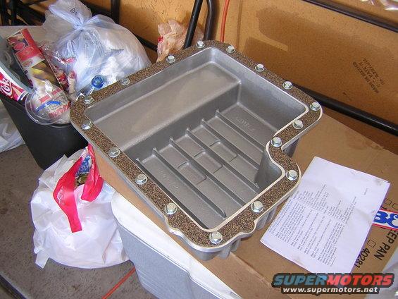 Aluminum transmission pan with gasket and bolts, next to trash bags and a document
