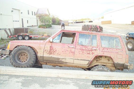 1988 Jeep Cherokee with large tires on an obstacle, covered in mud