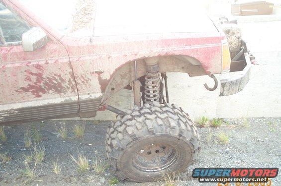 Mud-covered red SUV with large off-road tires and lifted suspension. Front passenger side wheel is turned