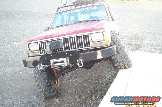 Red Jeep Cherokee with a winch and off-road tires, angled on a concrete barrier