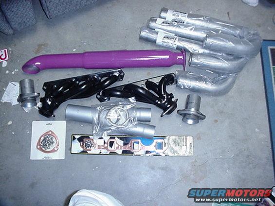 Various exhaust pipes, headers, and gaskets laid out on a concrete floor