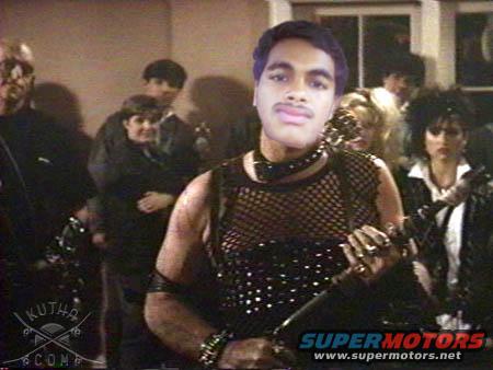Group of people in dark clothing, one man in foreground with a superimposed face and mesh shirt