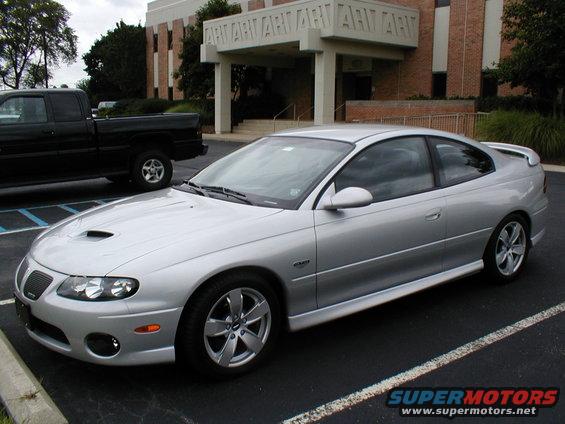 Silver Pontiac GTO coupe parked next to a black pickup truck in front of a brick building
