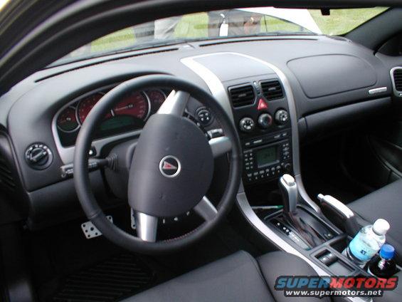 Car interior showing dashboard, steering wheel, center console with automatic shifter, and cupholders with drinks