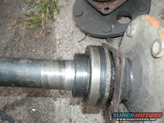Close-up of a vehicle's axle shaft with a bearing and hub assembly attached, resting on the ground