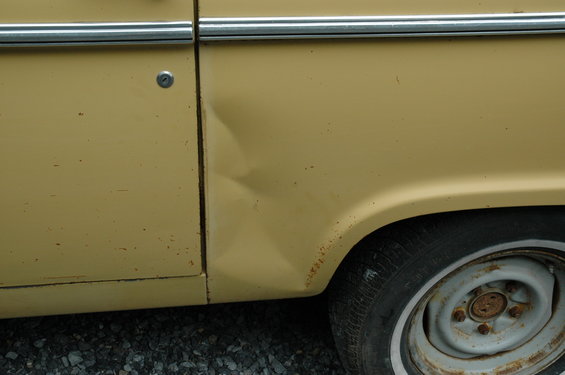 Yellow 1972 Ford Bronco side panel with dent and rust near wheel well
