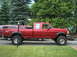 1996 Ford F-250 - A red crew cab pickup truck is parked in front of a residential setting with trees in the background.