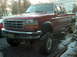 1996 Ford F-250 - This red 1996 Ford F-250 pickup truck is shown from a three-quarter front angle, lifted with large tires.
