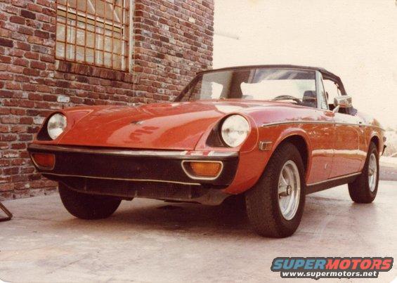 Red convertible sports car parked against a brick wall, front 3/4 view