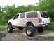 2000 Ford Excursion - A mud-splattered white Ford Excursion with oversized tires sits off-road.
